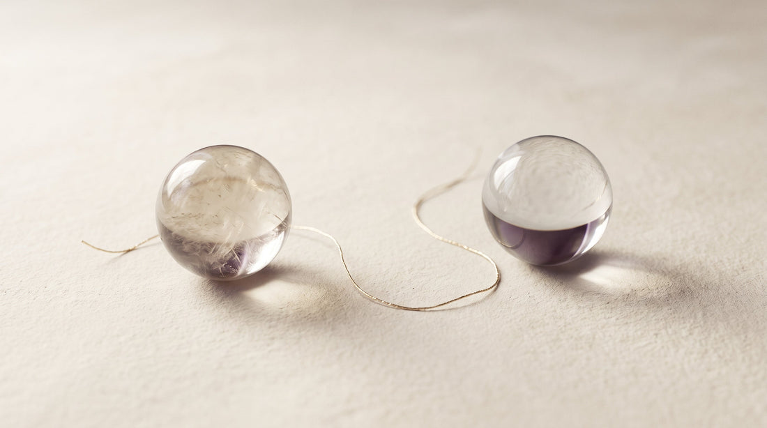 Two glass spheres connected by a fine golden thread on a cream surface